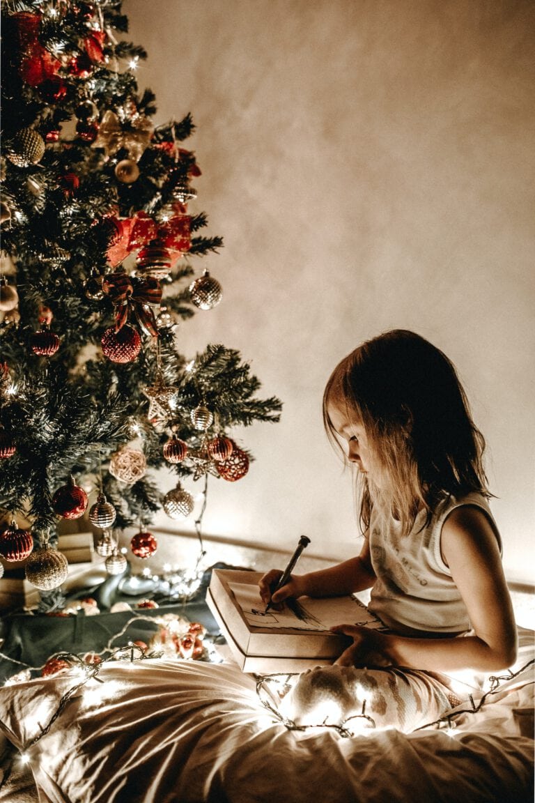 Kind sitzt vor Weihnachtsbaum